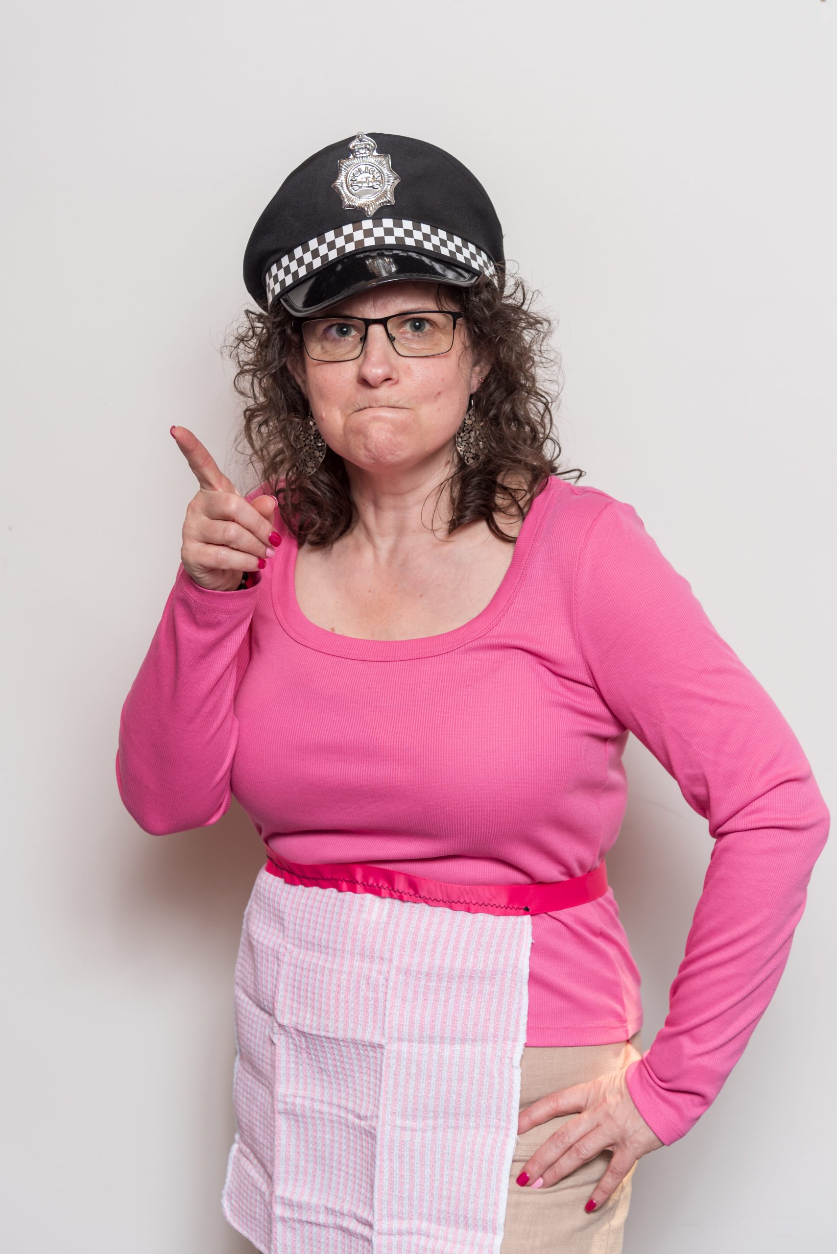 PoliceMum Point - Eva Rado image of Eva wearing an apron and a police cap, scowling and pointing