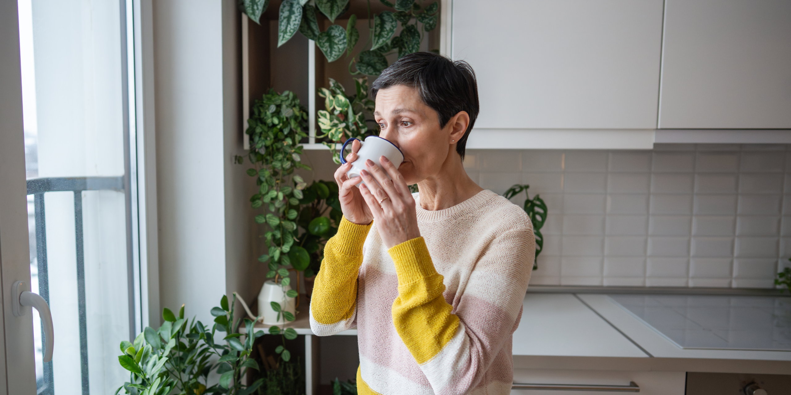GOOGLE Blog reflective Mum - Eva Rado Mother standing in her kitchen holding a coffee cup and reflecting quietly at home